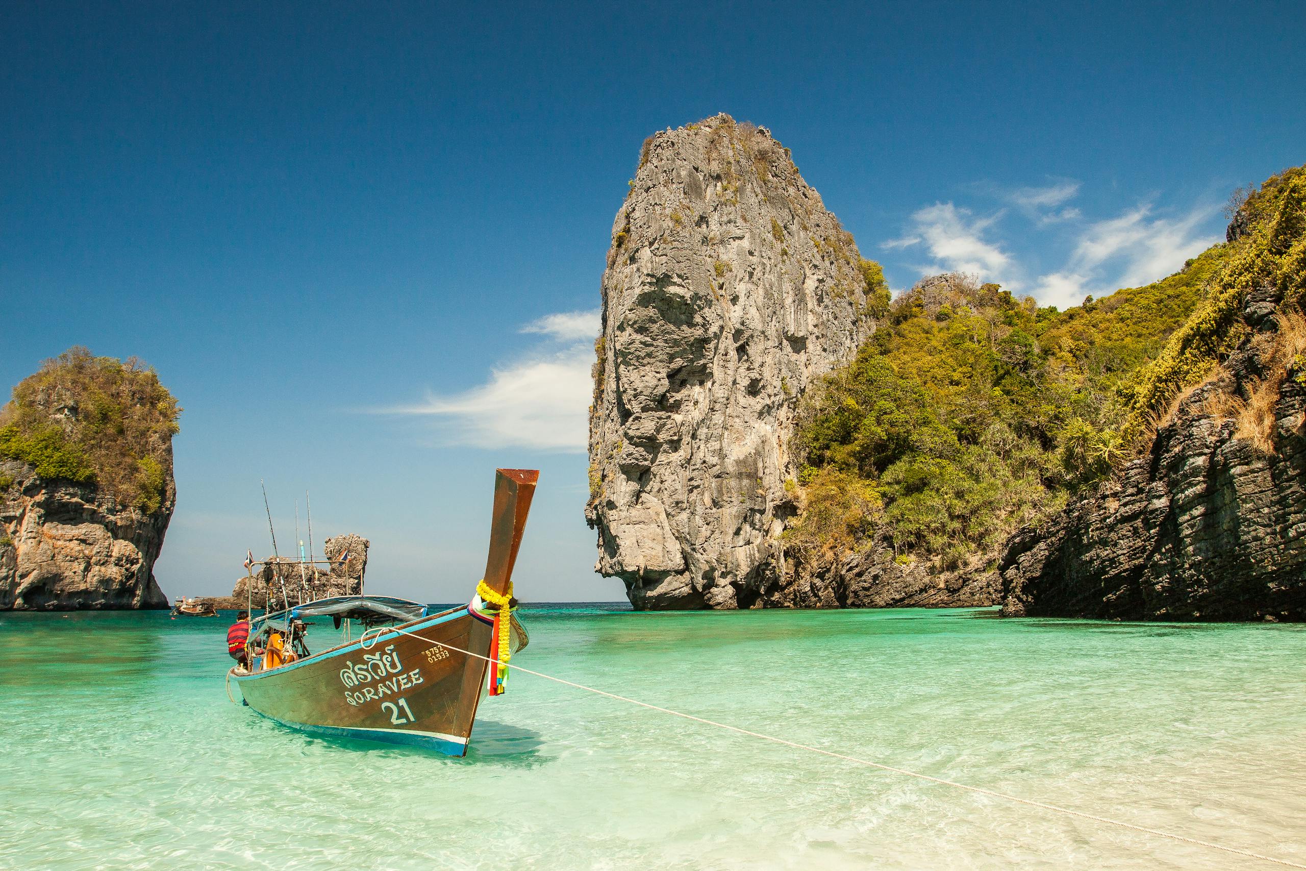 A picturesque tropical beach with a traditional boat and stunning limestone cliffs in clear turquoise waters.