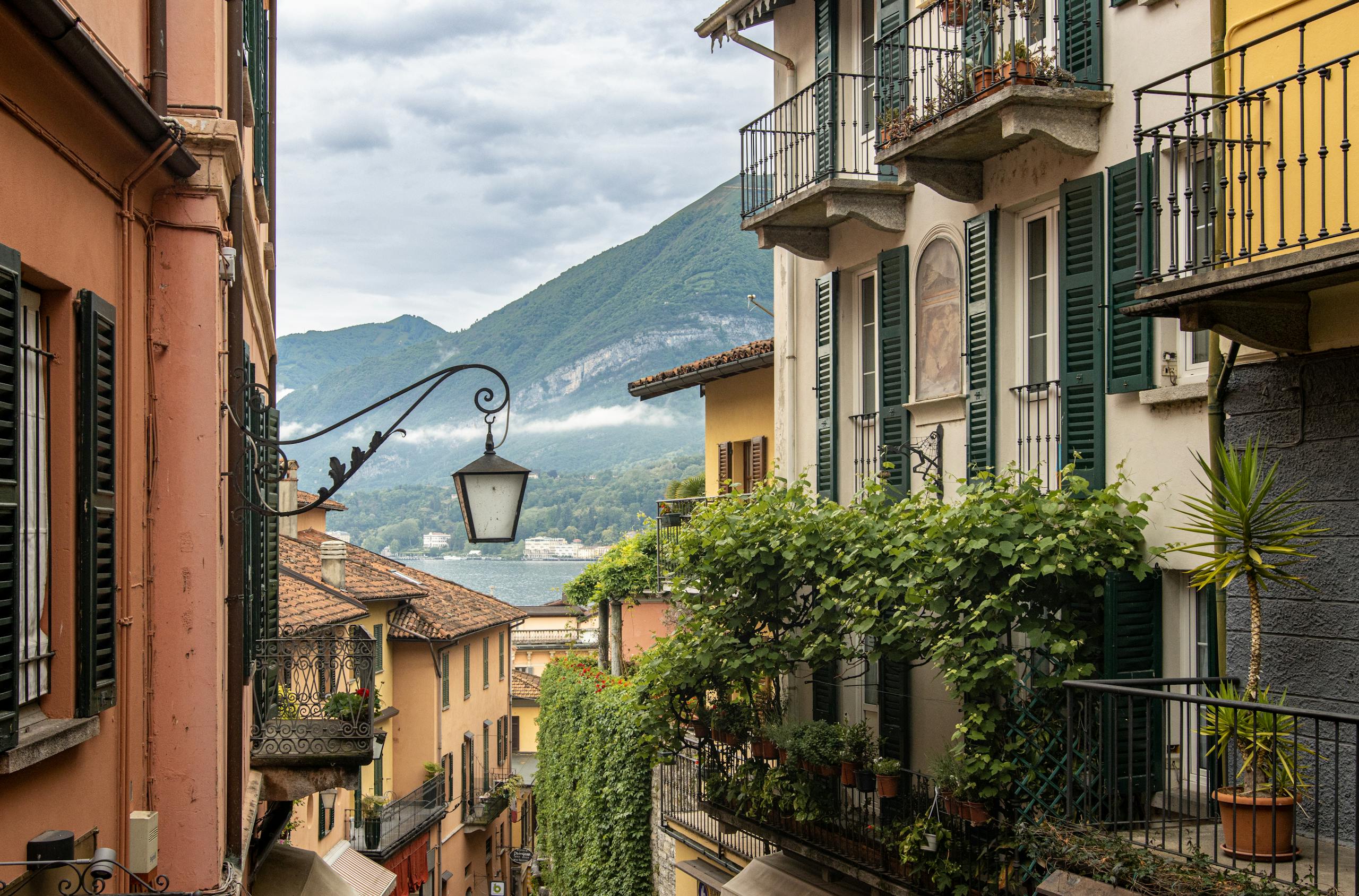 Picturesque Italian street with ornate balconies and a mountain in the backdrop.